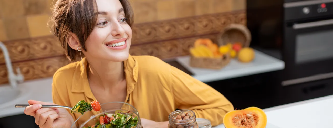 Femme sourit en mangeant une assiette de légumes crus