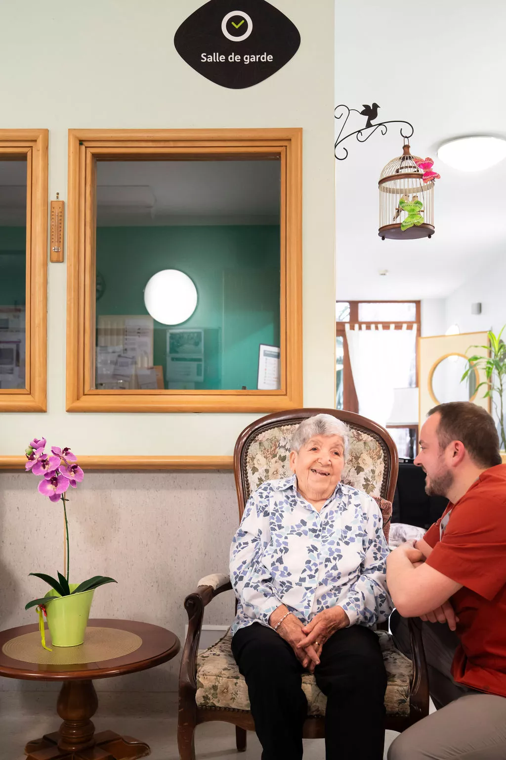 Femme âgée dans un fauteuil discutant avec un homme plus jeune accroupi